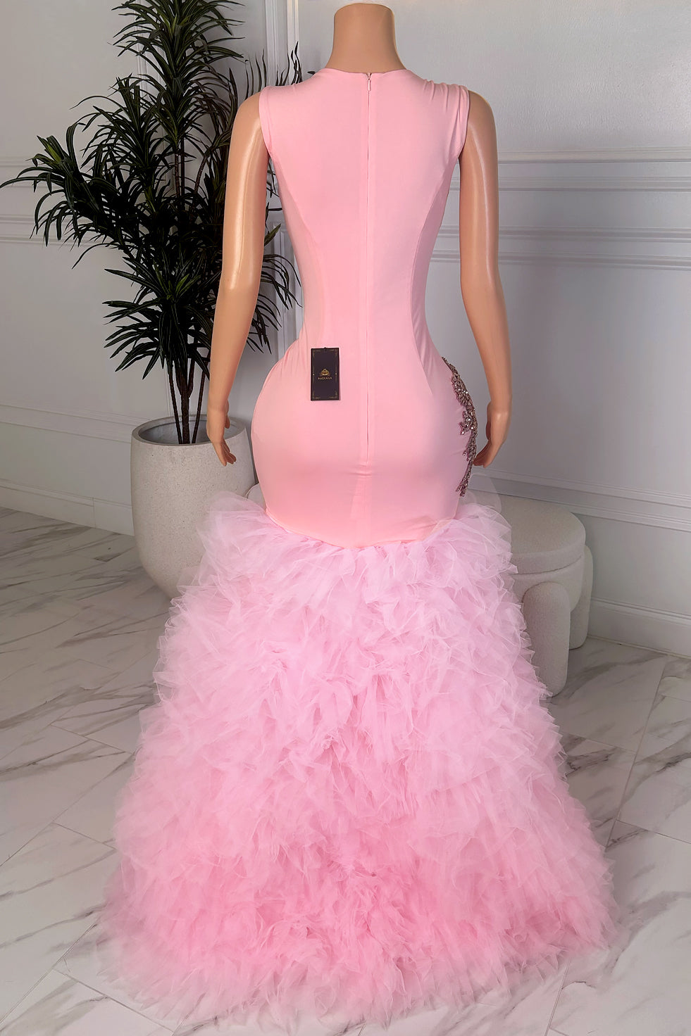 Back view of a blush pink fitted dress with a dramatic feathered lower hem and clean sleeveless silhouette