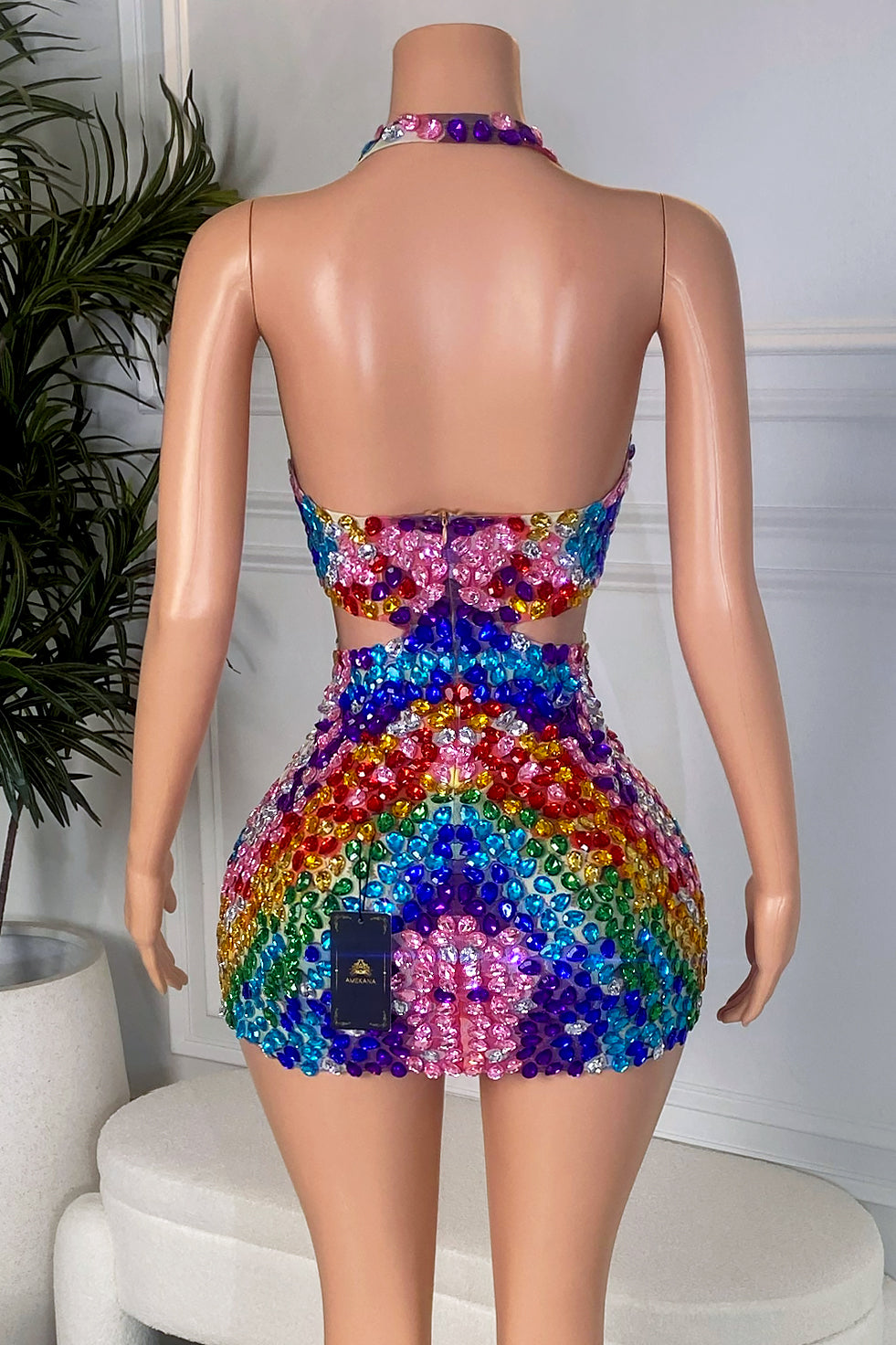 Back view of a multicolor crystal mini dress with an open back, halter neckline, fitted skirt, and colorful jewel-style embellishments.