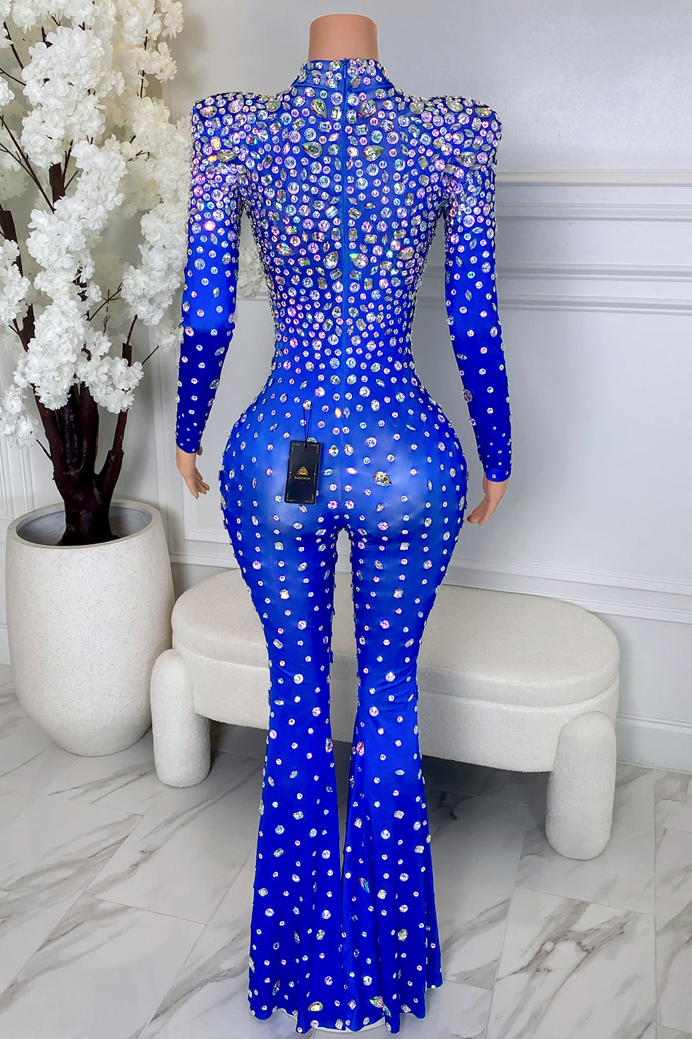 Back view of Milan blue rhinestone jumpsuit with long sleeves, padded shoulders, back zipper closure, allover rhinestones, and flared leg fit