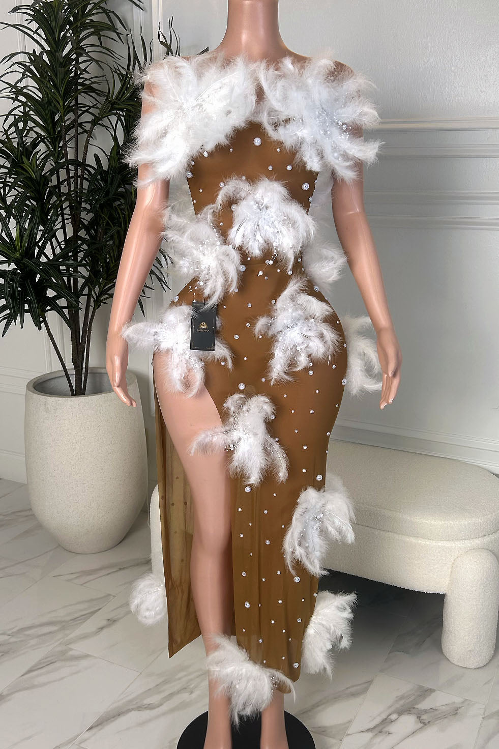 Nude illusion mesh maxi dress with white feather trim, pearl embellishments, and high slit on mannequin, front view.