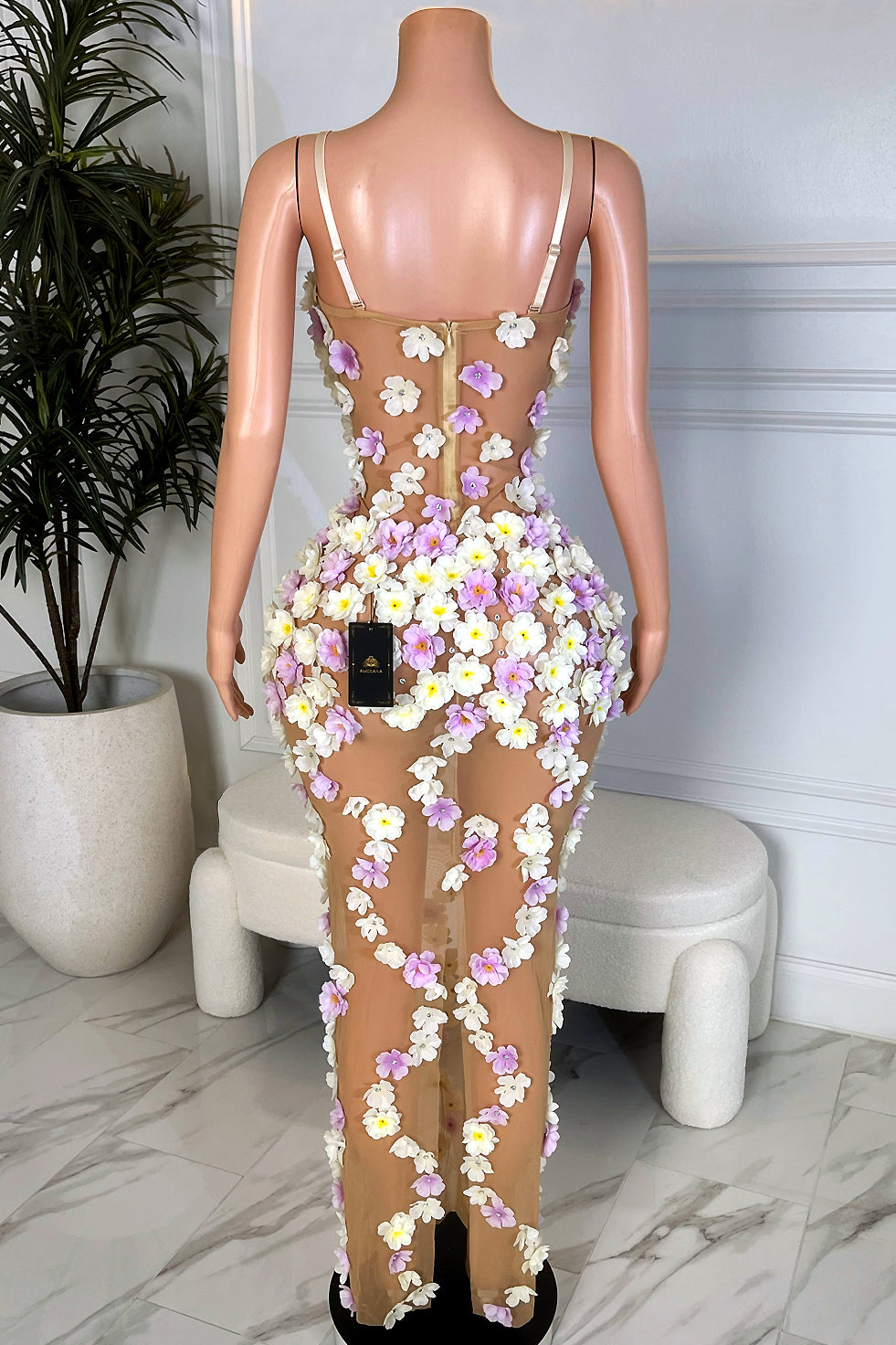 Back view of nude floral mesh maxi dress with pastel flower appliqués cascading down the legs, shown on mannequin in studio setting