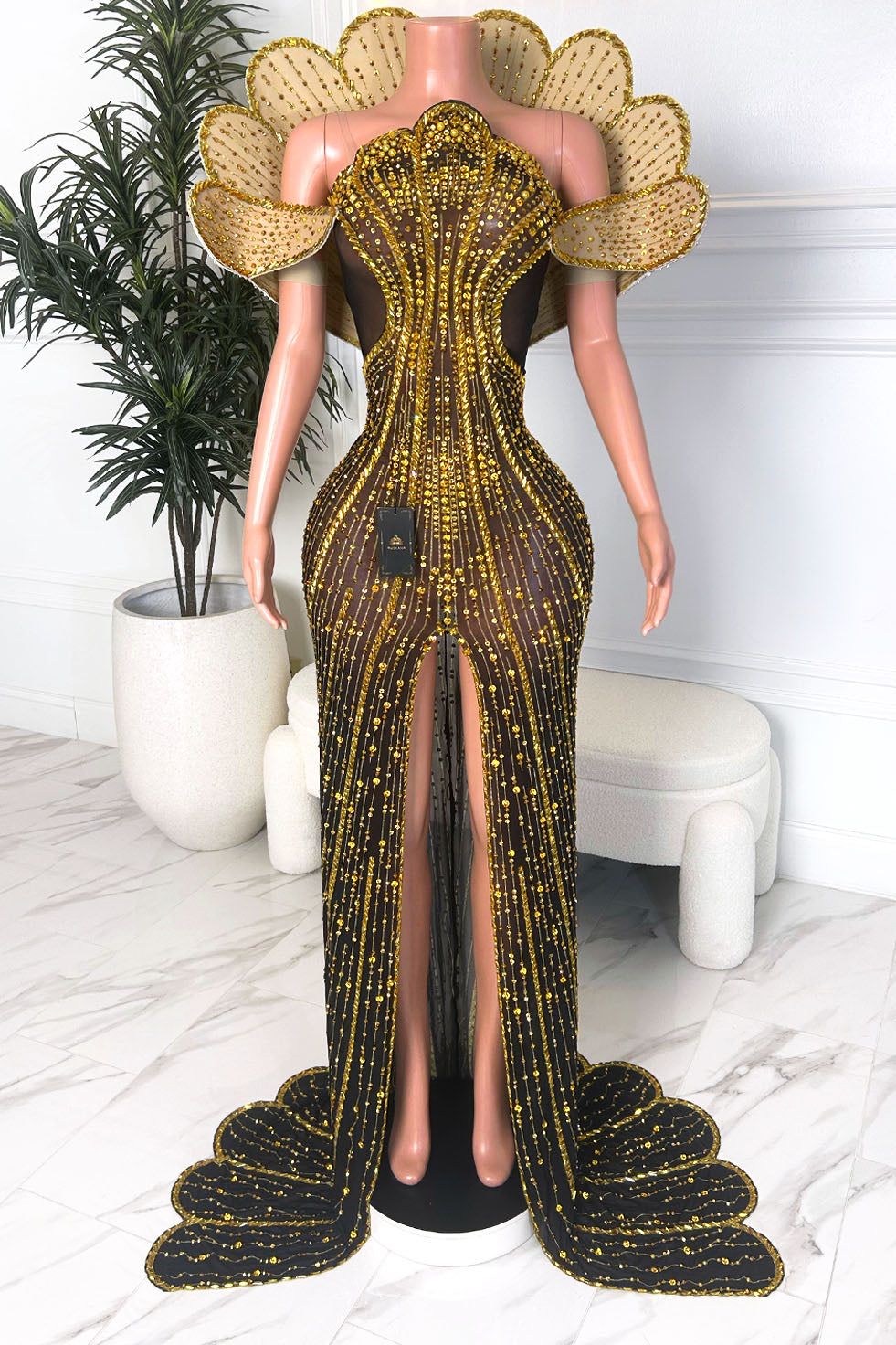 Front view of a black sheer couture gown with gold embellishment, shell inspired bodice, off shoulder panels, and front slit