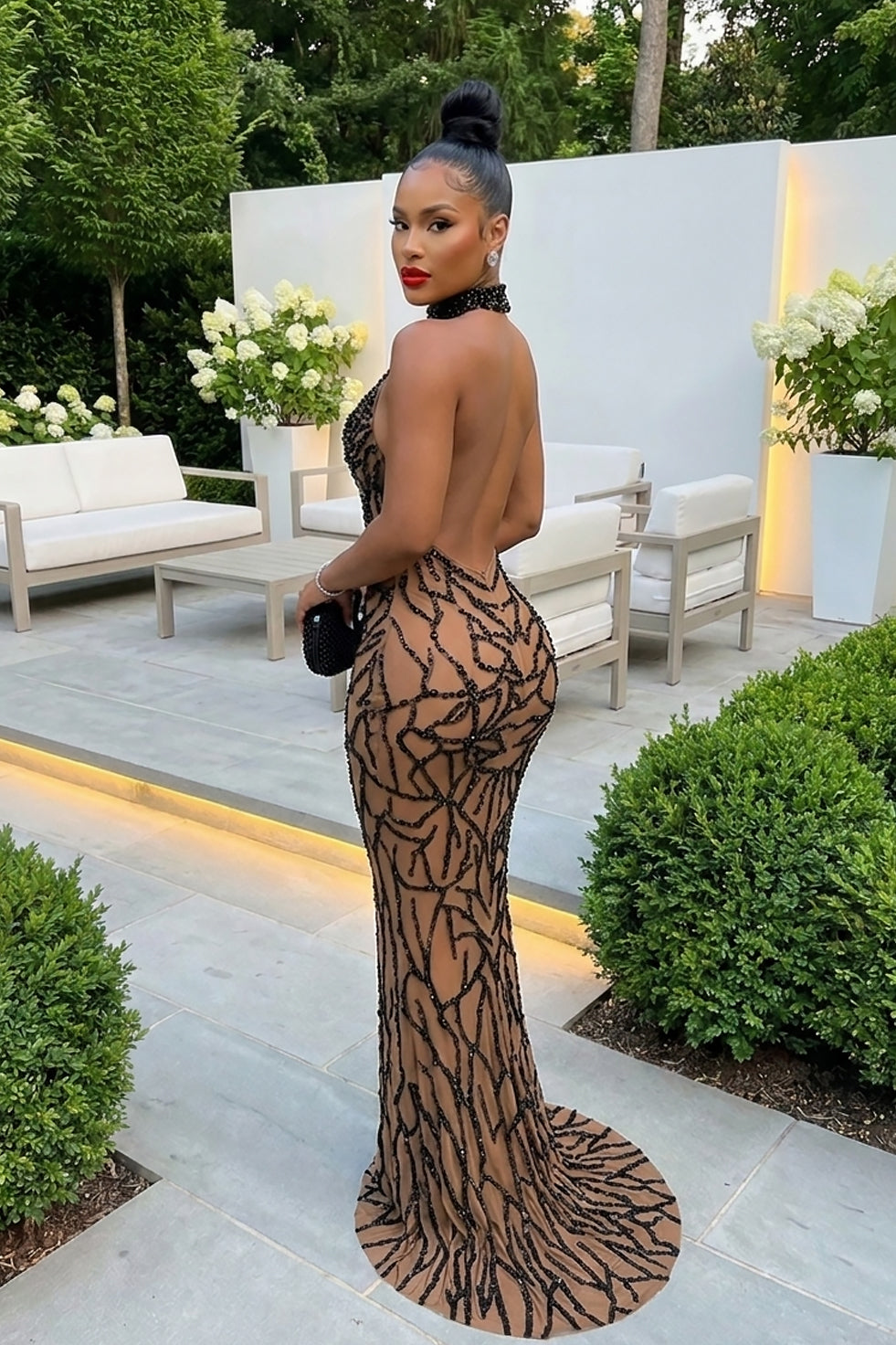 Side view of a model wearing a nude illusion halter dress with black abstract embellishment and open back detail