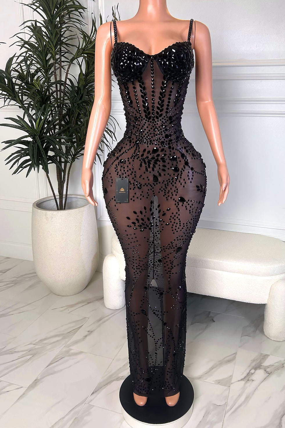 Front view of a black rhinestone illusion maxi gown with a structured embellished bust, slim straps, sheer mesh fabric, and swirling glossy black crystal detailing