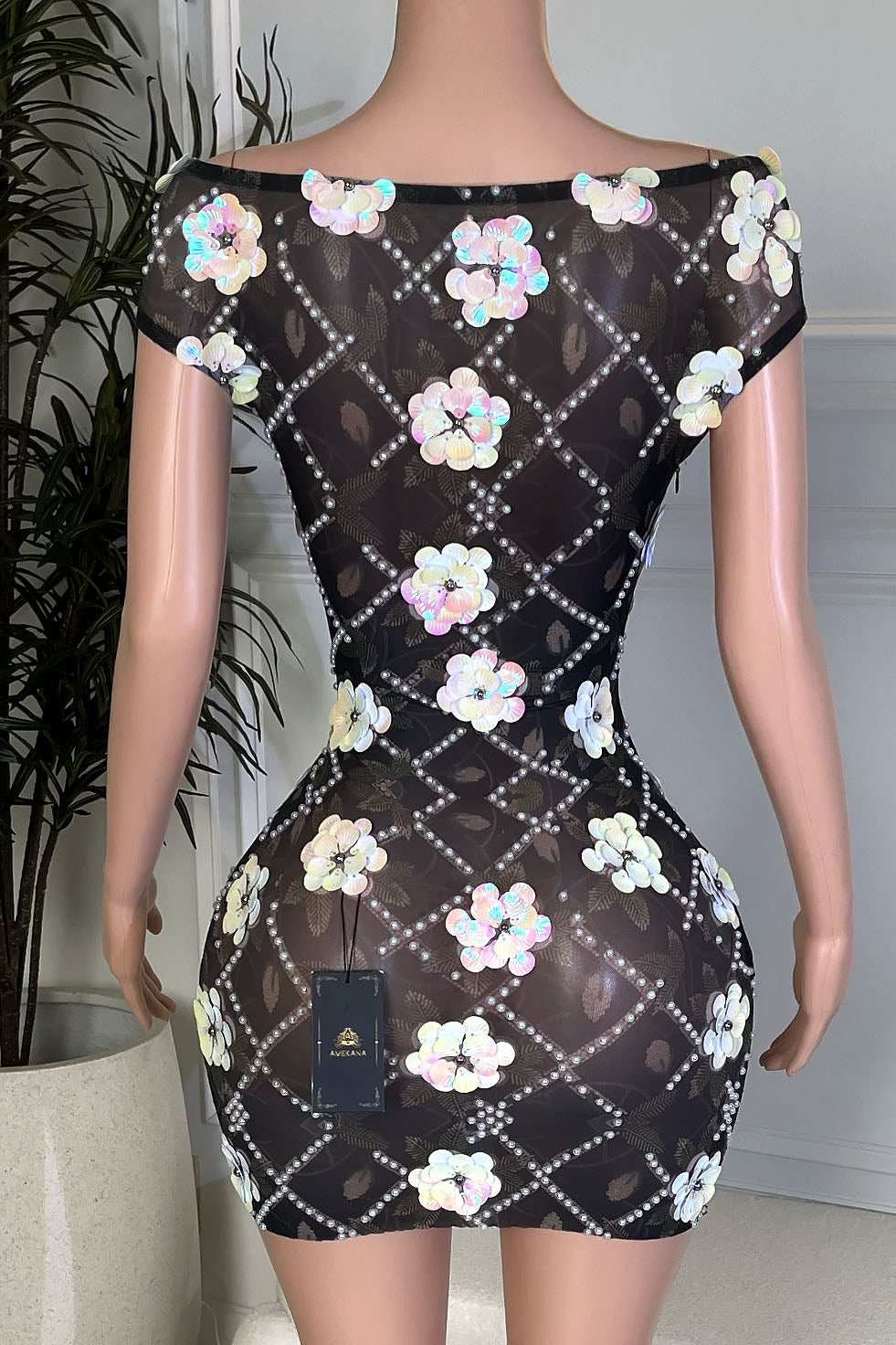 Back view of black sheer off shoulder bodycon mini dress featuring rhinestone lattice pattern and iridescent floral sequin appliqués