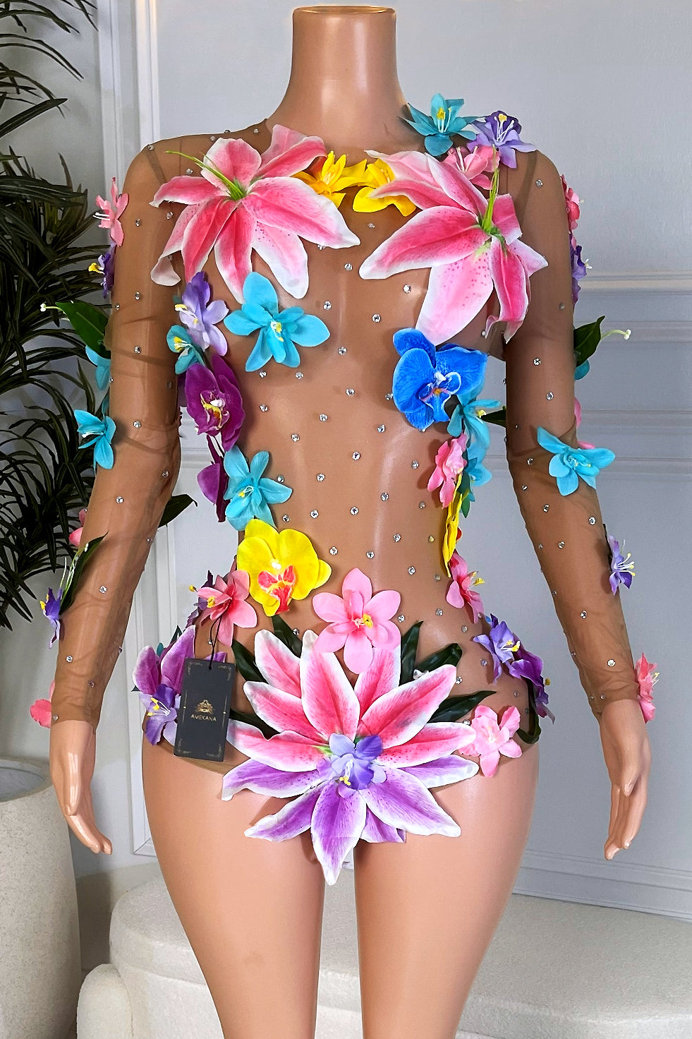 Nude mesh long sleeve playsuit covered in bright 3D pink, purple, blue, and yellow flowers with rhinestones on a mannequin, front view