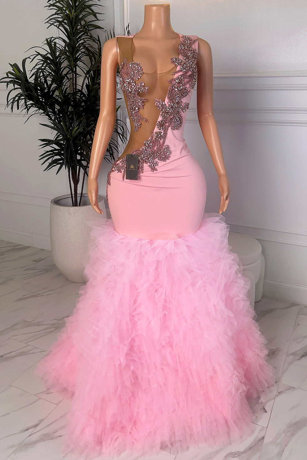 Front view of a blush pink dress with sheer illusion cutouts, crystal floral embellishment, and a voluminous feathered hem