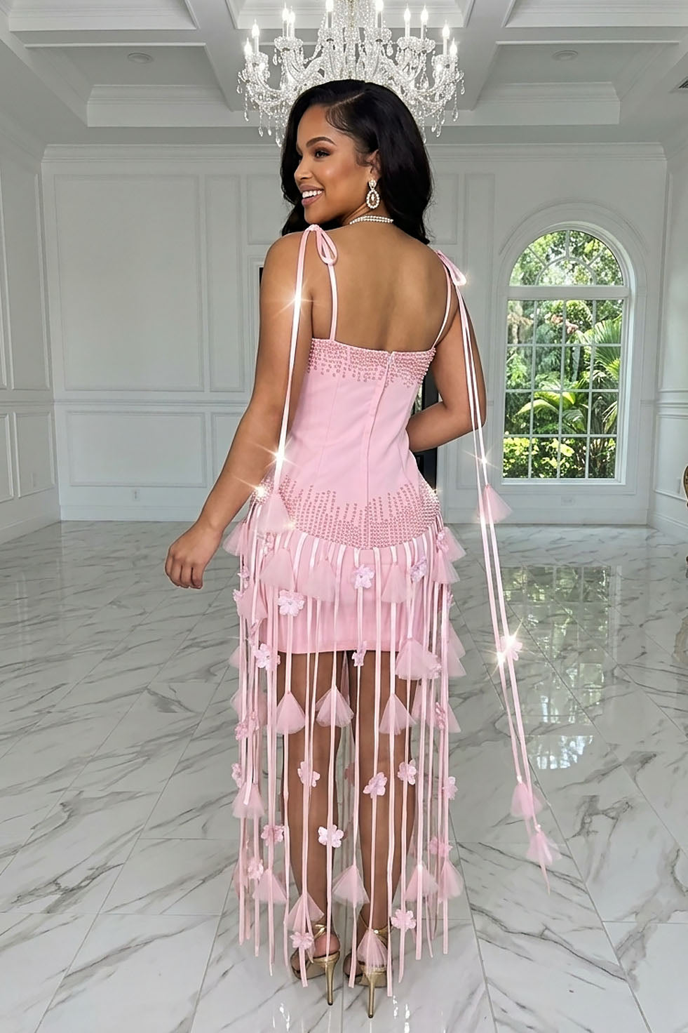 Back view of a pink dress with tie shoulder straps, back zipper closure, and long fringe adorned with floral-style accents