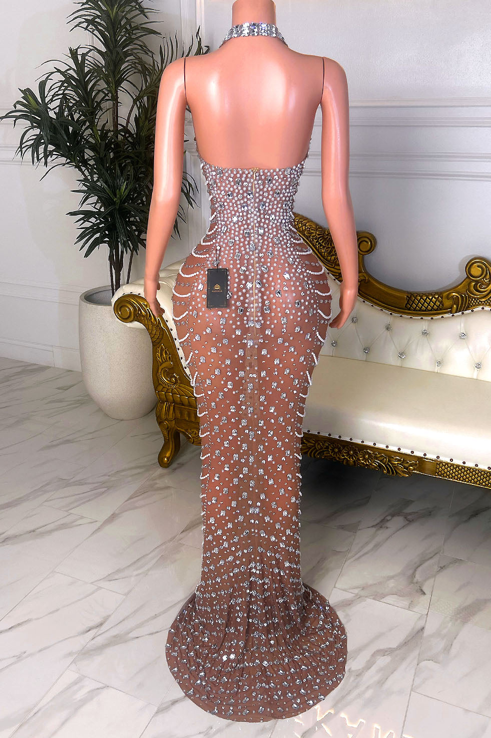 Back view of a nude illusion silver crystal gown with an open back, halter choker-style strap, back zipper closure, and floor-length silhouette