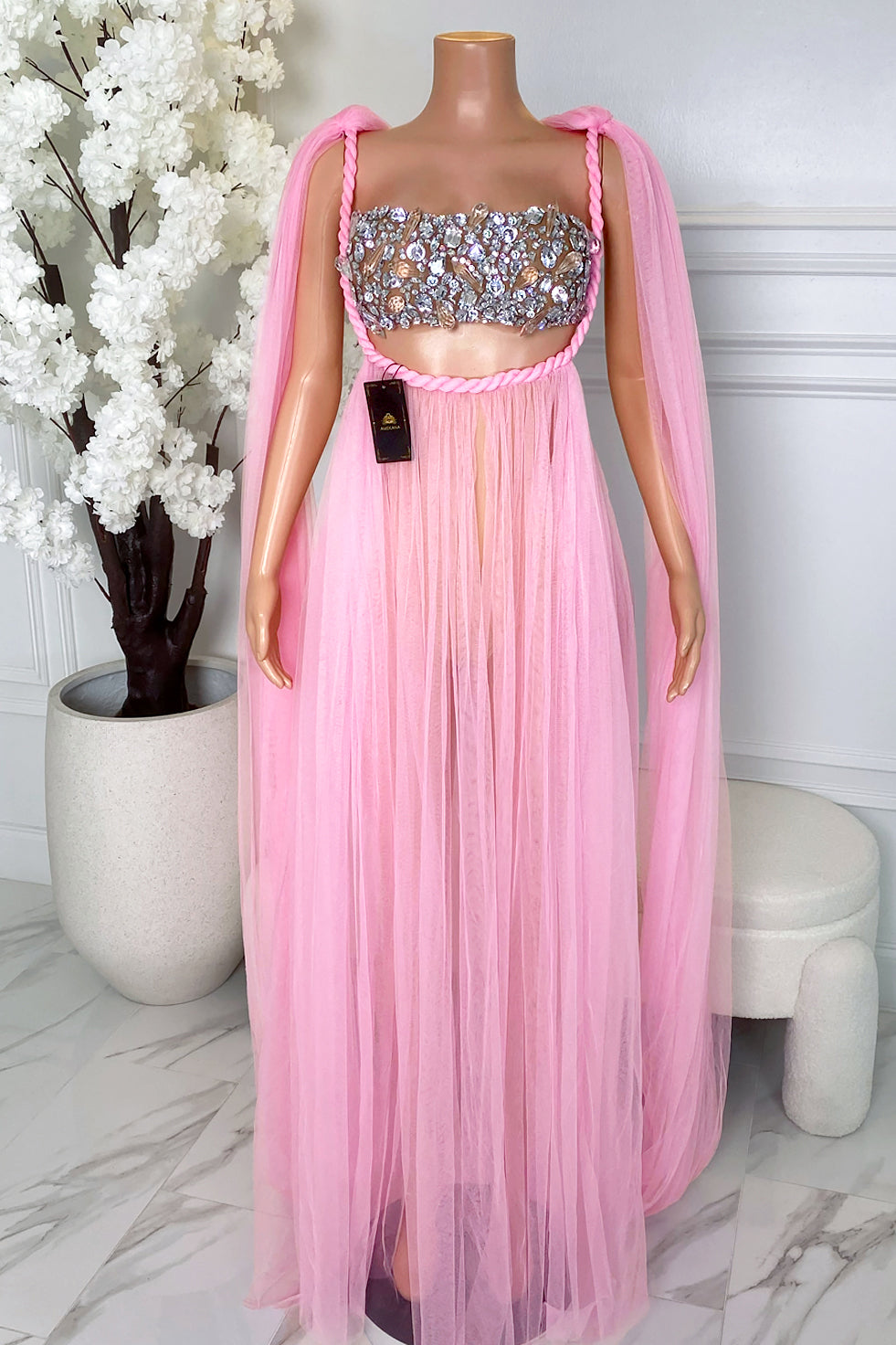 Front view of Elara Pink Rhinestone Tulle Maxi Dress featuring a sparkling rhinestone bustier top, braided pink trim, sheer pink tulle maxi skirt, and draped shoulder cape detail