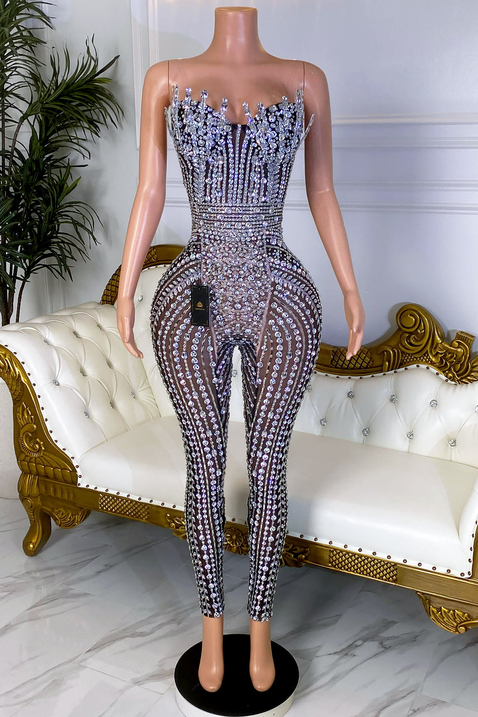 Back view of a black sheer mesh jumpsuit with silver crystal embellishments, clear strap details, structured corset bodice, and fitted pants.