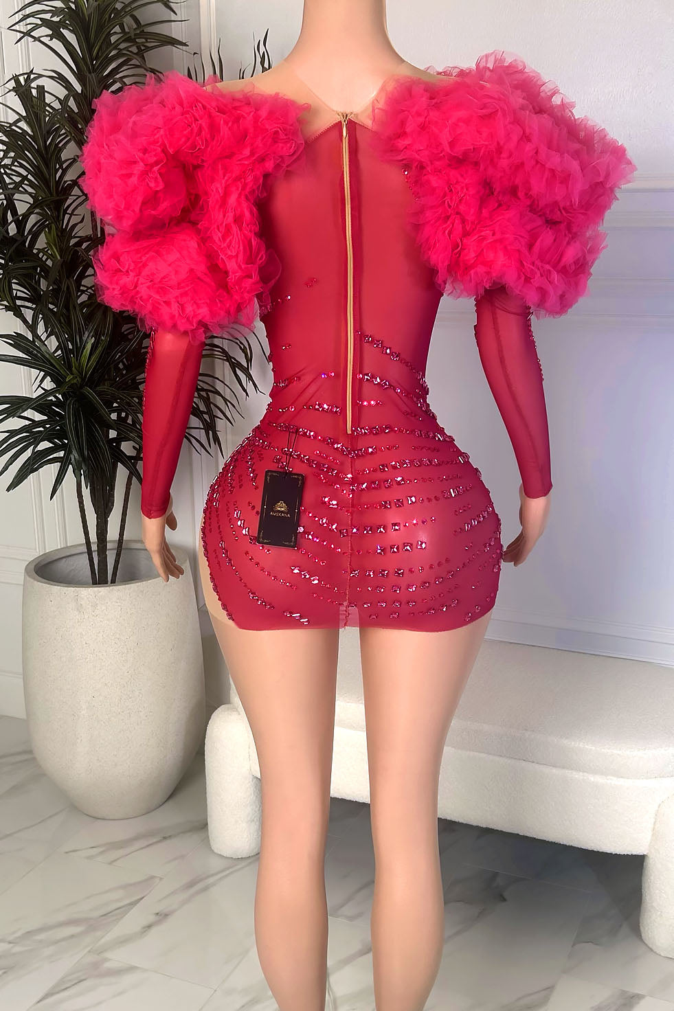 Back view of a hot pink mini dress with oversized tulle shoulder ruffles, sheer back panel, long sleeves, and back zipper closure