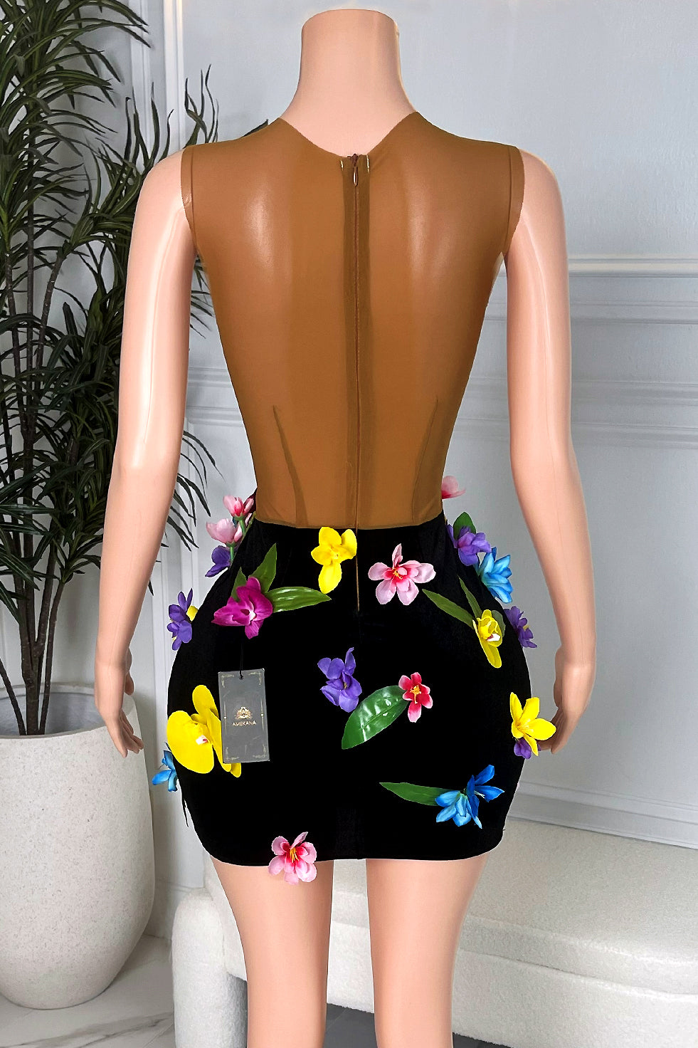 Back view of a brown illusion mesh and black velvet mini dress with multicolor 3D flowers and back zipper, displayed on a mannequin in a marble floor boutique.