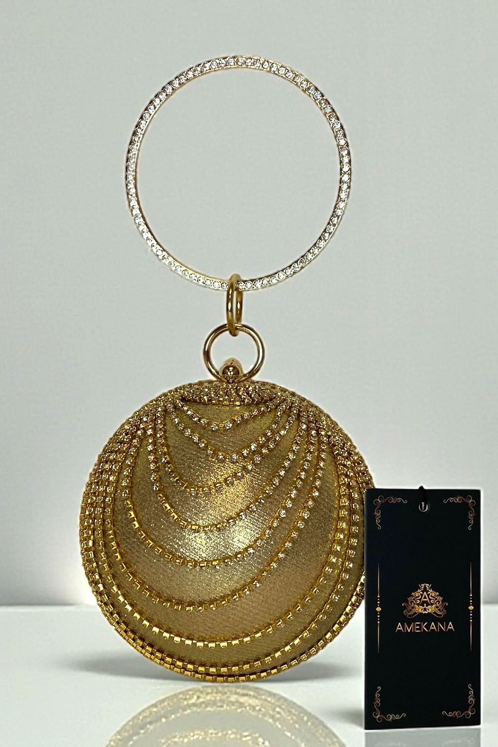 Gold globe rhinestone clutch with jeweled circle handle ring and layered crystal chain drape on white background