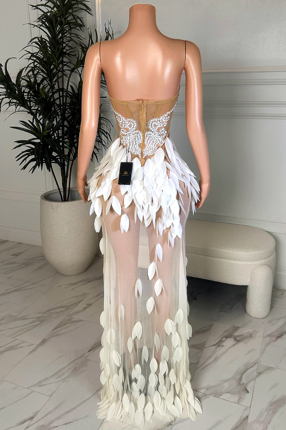 Back view of a white petal maxi dress with a semi-sheer corset back, slim straps, center zipper closure, and cascading petal appliqué