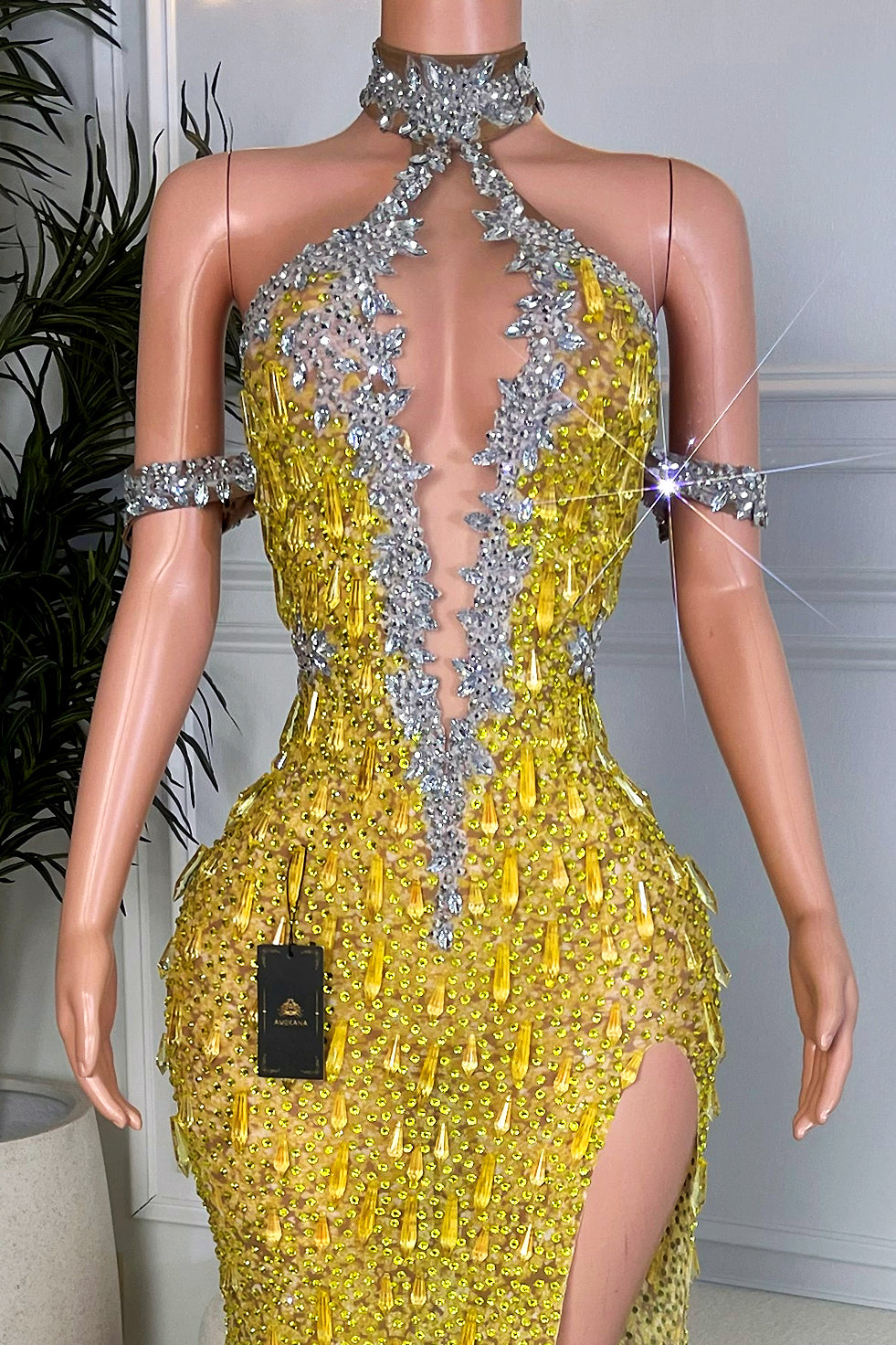 Close-up bodice detail of Krystal yellow rhinestone maxi dress showing silver crystal appliqué trim, illusion plunge neckline, and yellow rhinestone embellishments.