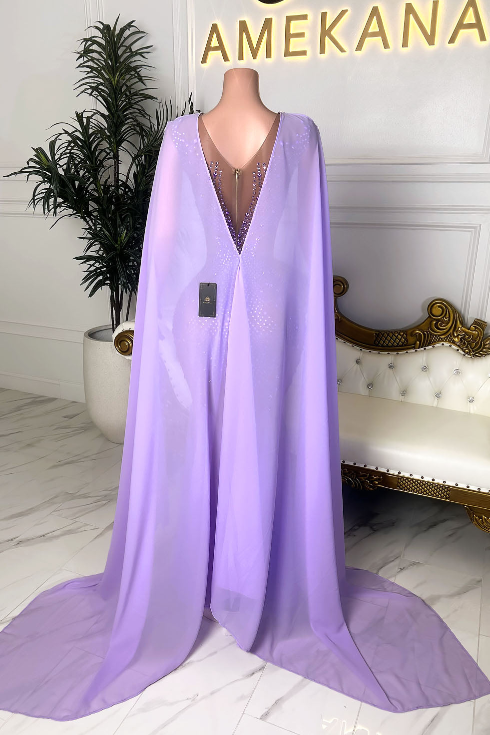 Back view of a lavender crystal embellished gown with a deep illusion V back, center zipper closure, and long flowing cape train