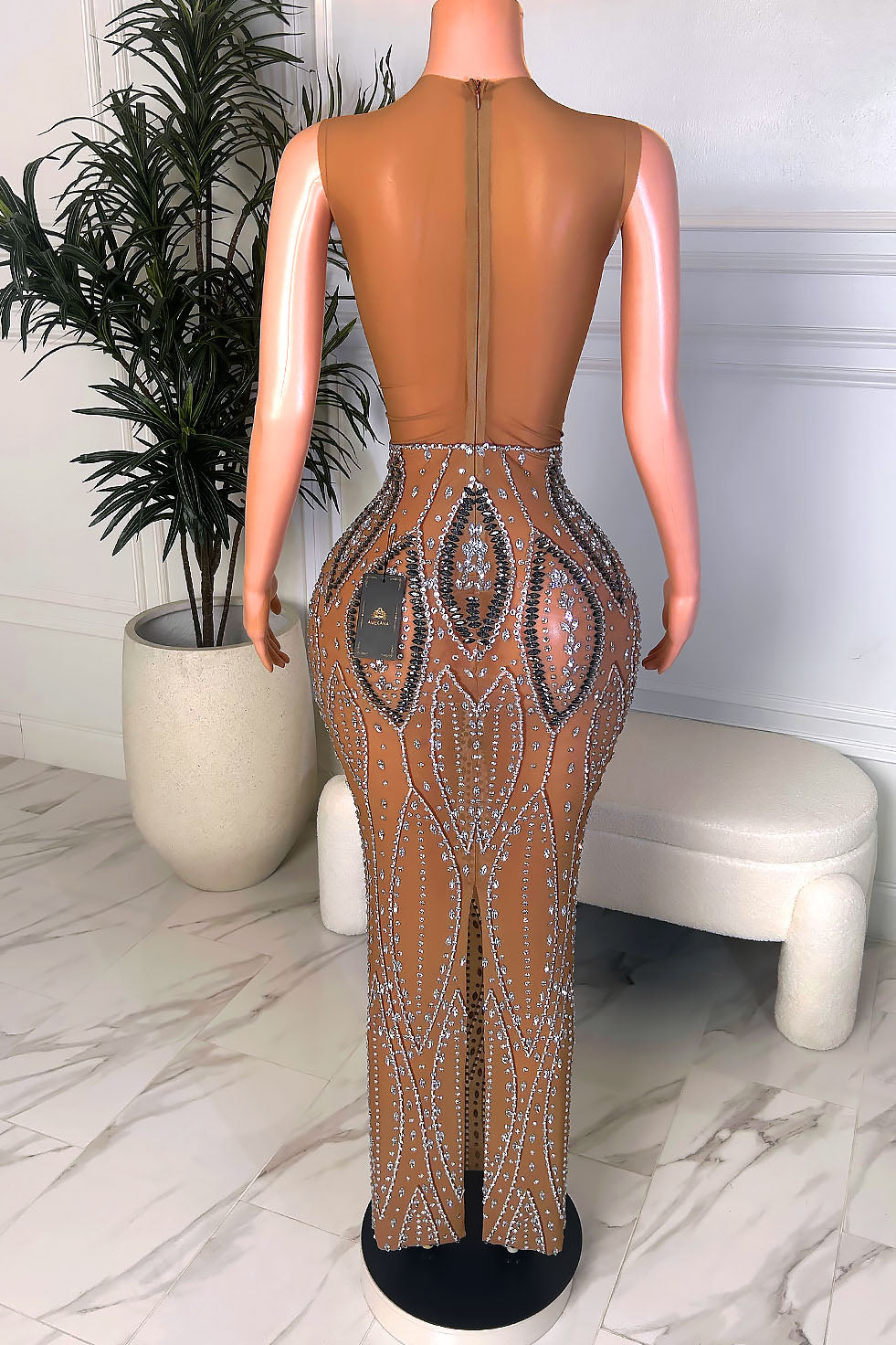 Back view of a nude illusion crystal embellished gown with a full illusion back, back zipper closure, and rear slit detail