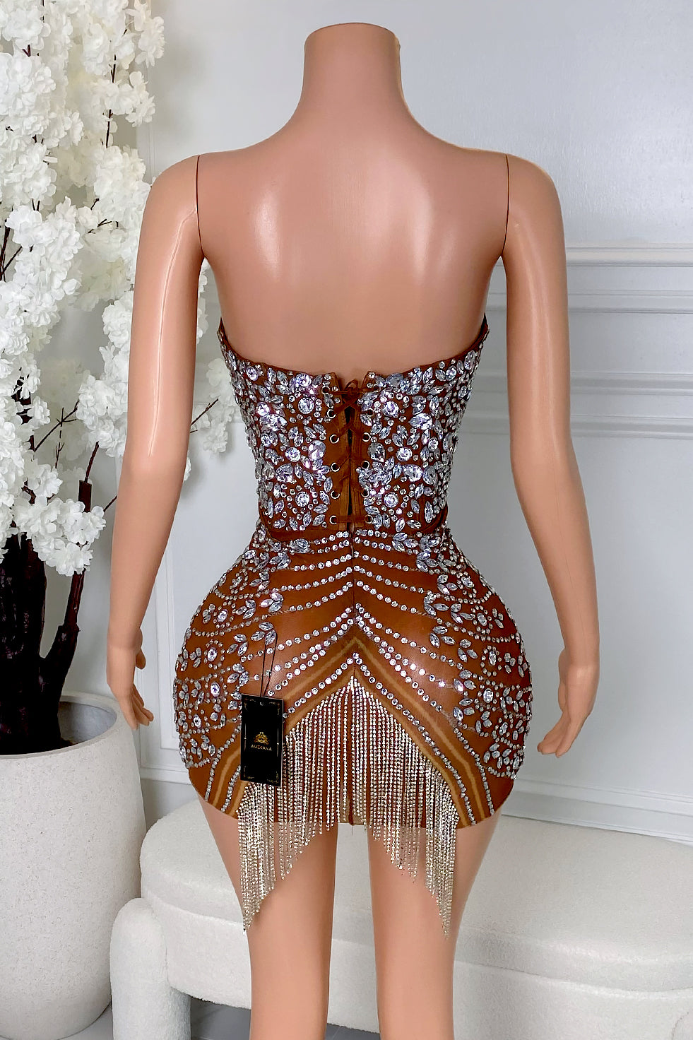Back view of brown sheer mesh rhinestone mini dress with lace-up closure, silver rhinestone detailing, rhinestone fringe hem, and body-hugging mini fit