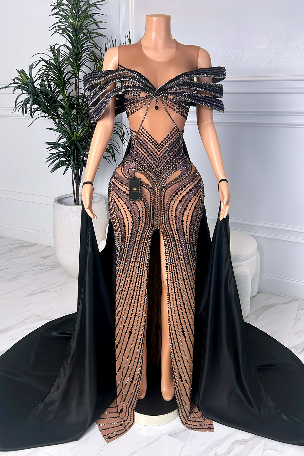 Front view of black illusion dress with crystal embellishment, off-shoulder detail, front slit, and dramatic cape panels
