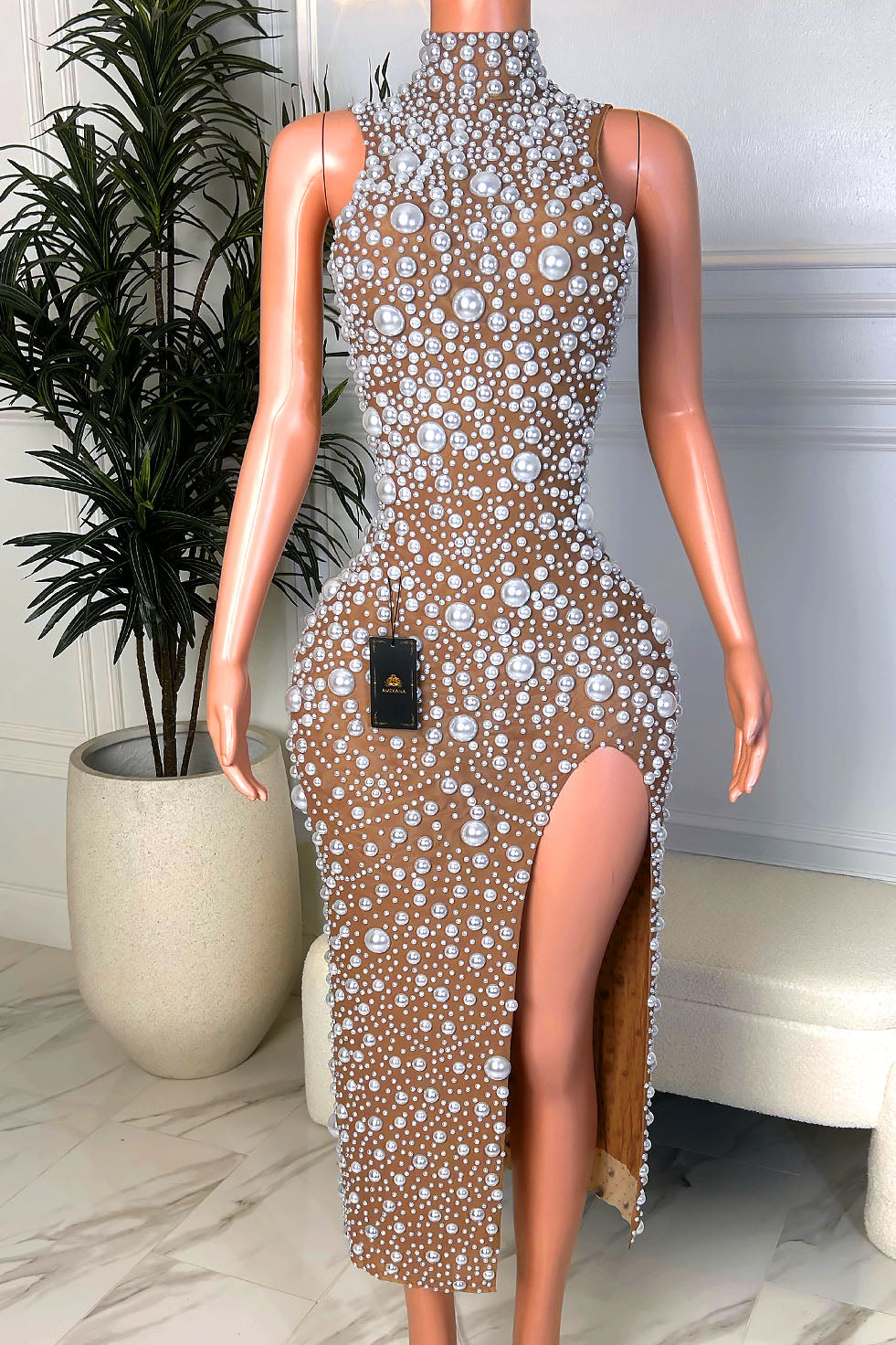 Front view of a nude illusion midi dress with a high pearl neckline, mixed-size pearl embellishments, and a dramatic front slit