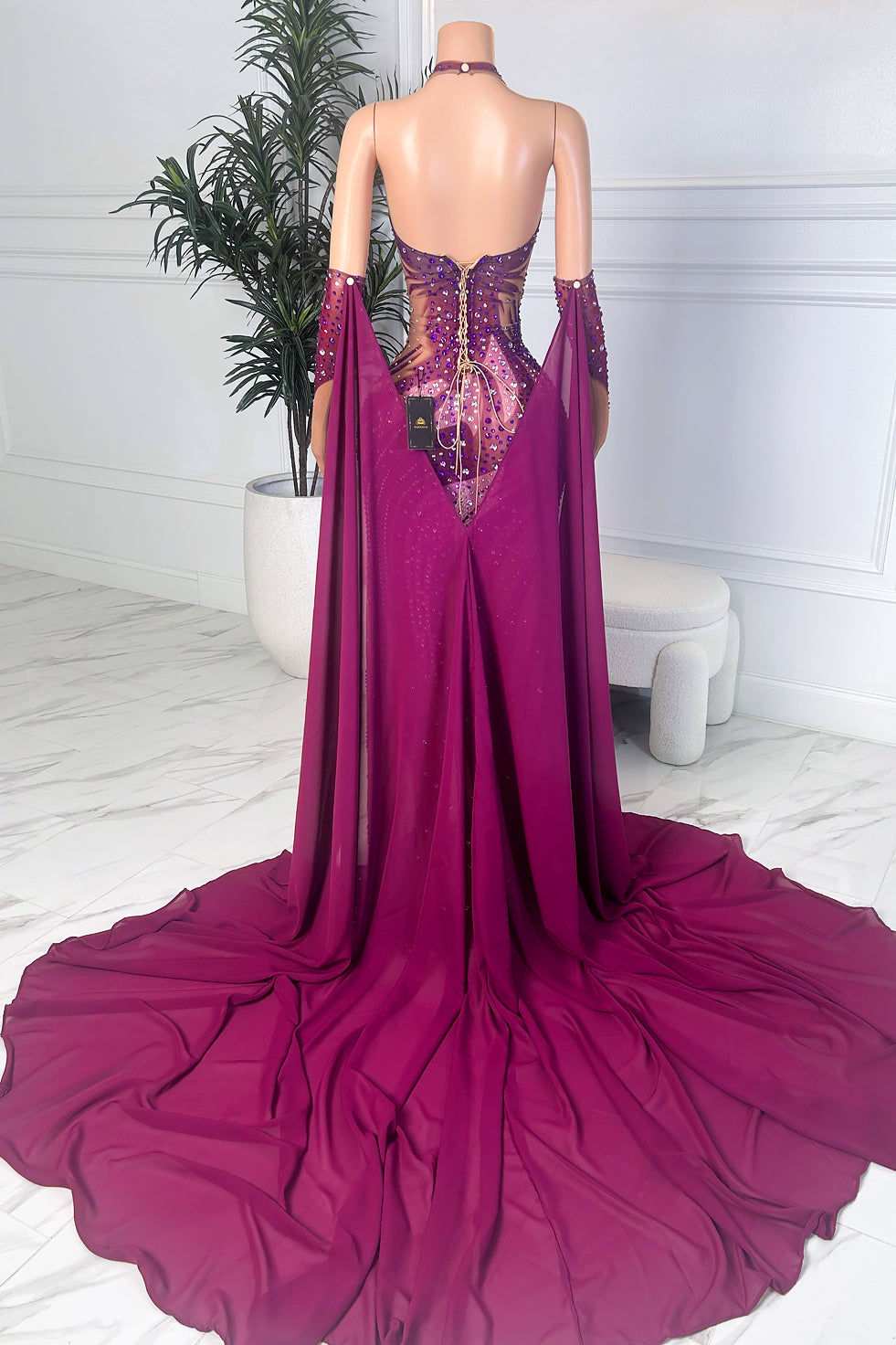 Back view of a purple halter dress on a mannequin with lace-up corset back and long cape-style drapes