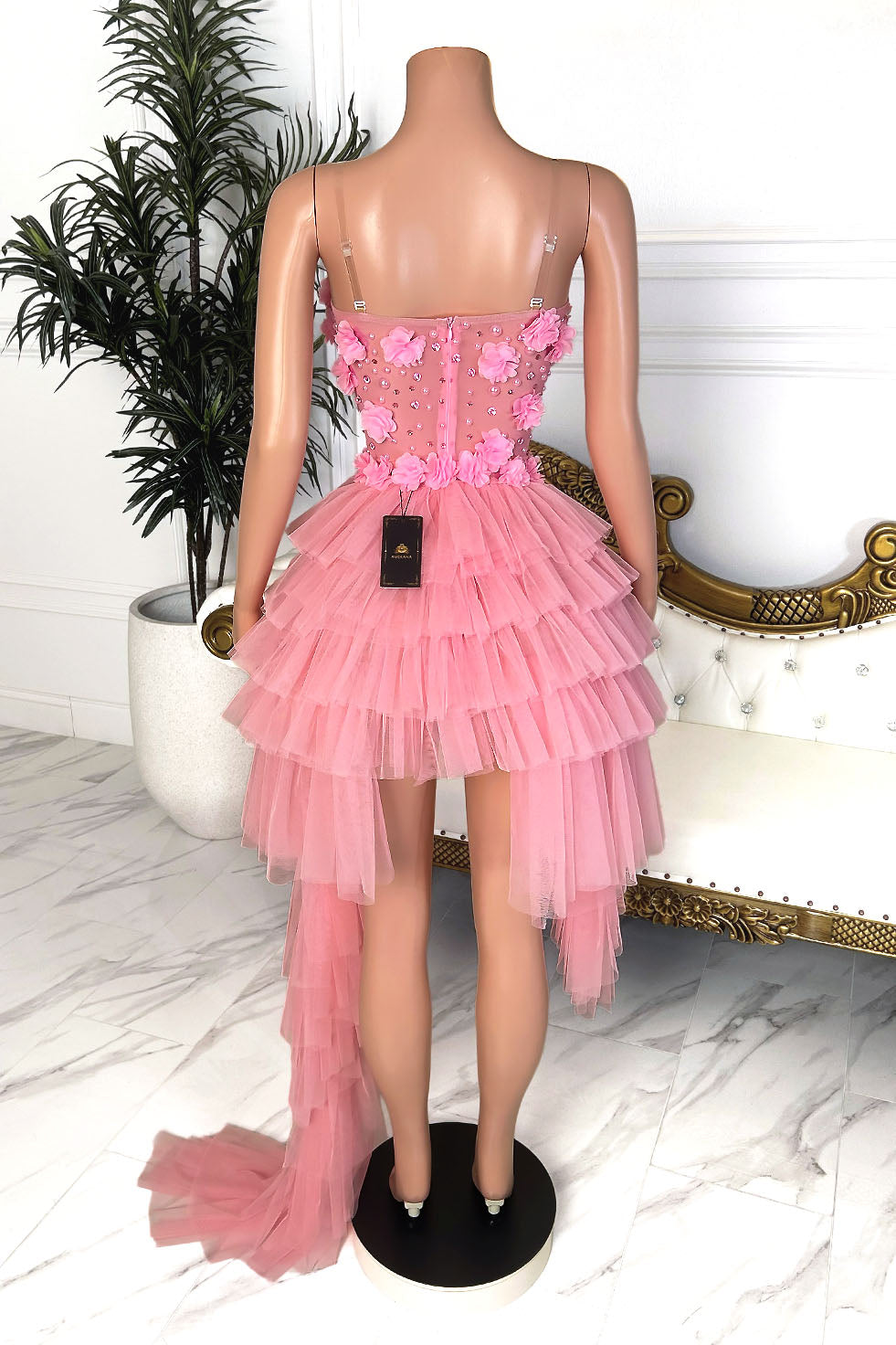 Back view of a blush pink high low mini dress with floral appliqués, rhinestone bodice, and cascading layered tulle panels