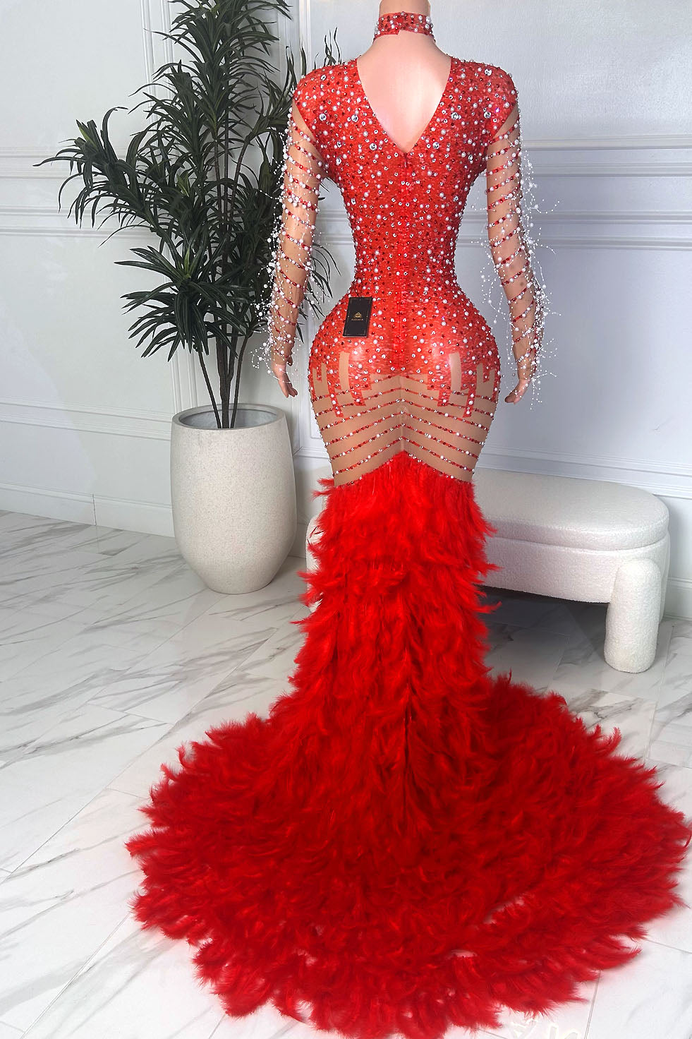 Back view of Ruby Royale Gown, a red crystal embellished gown with sheer detailing, V-back, and dramatic feathered train