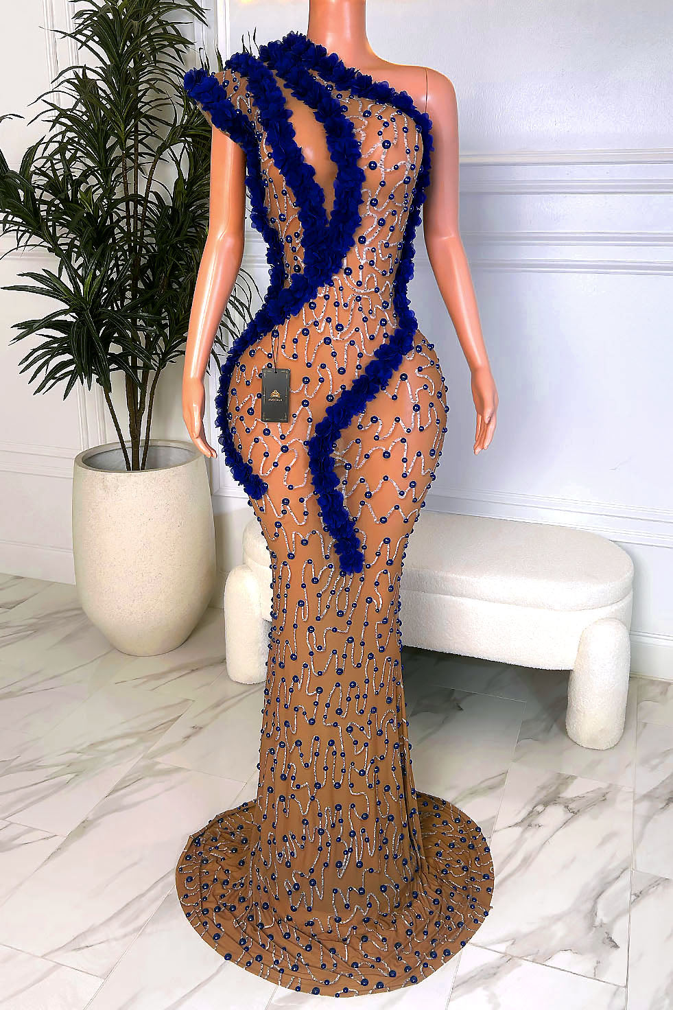 Nude illusion mesh mermaid maxi gown covered in royal blue rhinestones with bold 3D blue floral trim and a sweeping train, front view