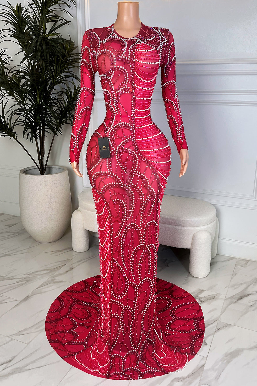 Front view of a hot fuchsia long sleeve mesh maxi gown with nude illusion base, covered in swirling rhinestone and diamante patterns and finished with a dramatic round train 