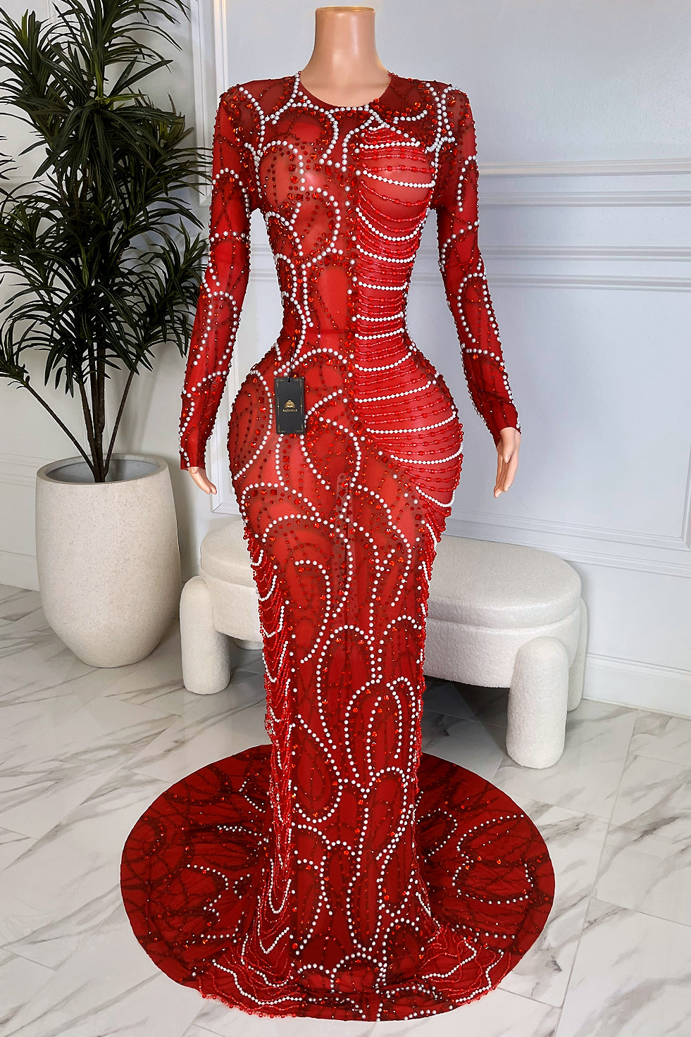 Front view of a long sleeve red rhinestone mesh maxi dress with bodycon fit and round train on mannequin in marble room