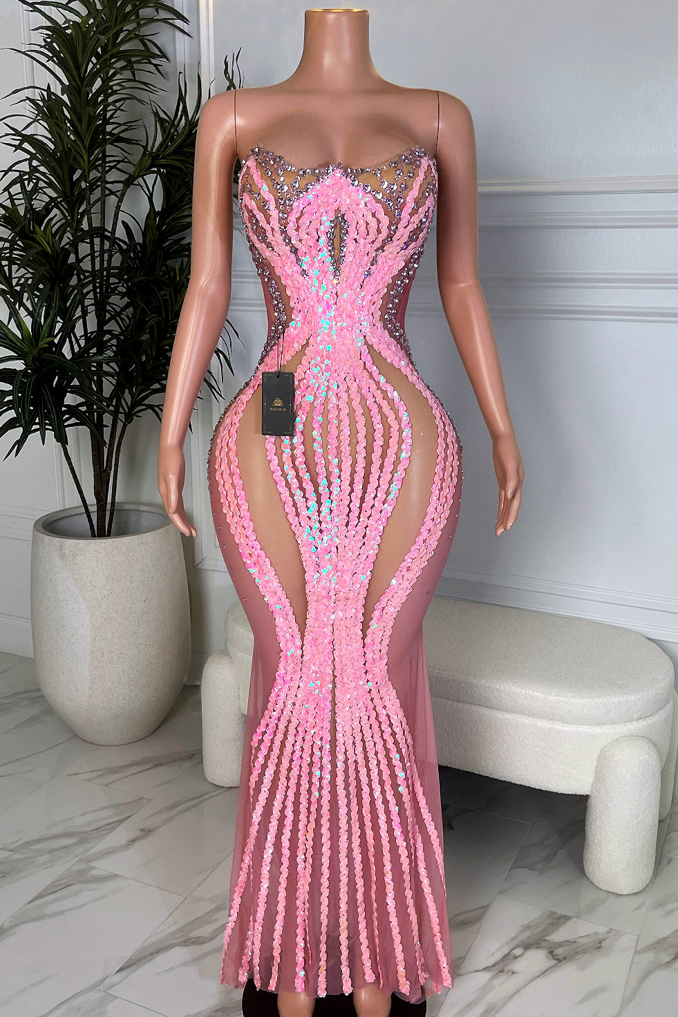 Front view of the Venus Wave Illusion Gown, a strapless nude mesh maxi dress with pink iridescent sequin waves creating an extreme hourglass shape, shown on a mannequin in a marble floor studio.