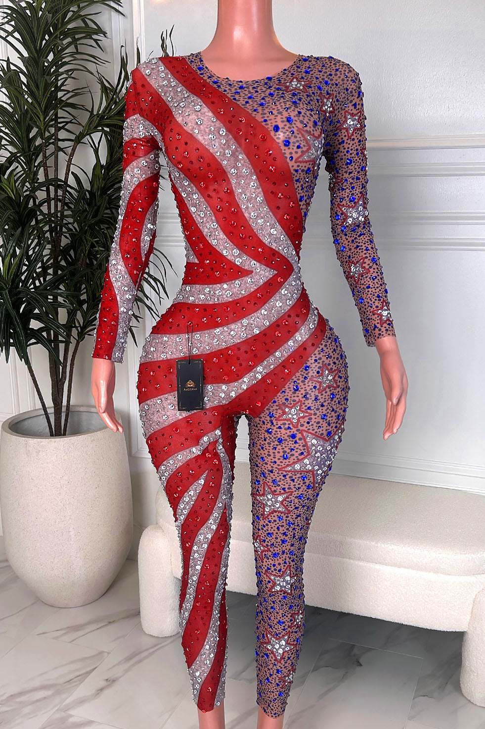 Back view of a nude illusion rhinestone jumpsuit with red and silver stripe detailing, star accents, and blue crystal sparkle on one leg.